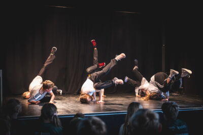 Gruppe aus 6 Jugendlichen macht eine Tanzperformance auf der Bühne vor Publikum.