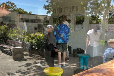 In einer Scheibe spiegeln sich Menschen von Außen und Innen die eine Ausstellung betrachten.